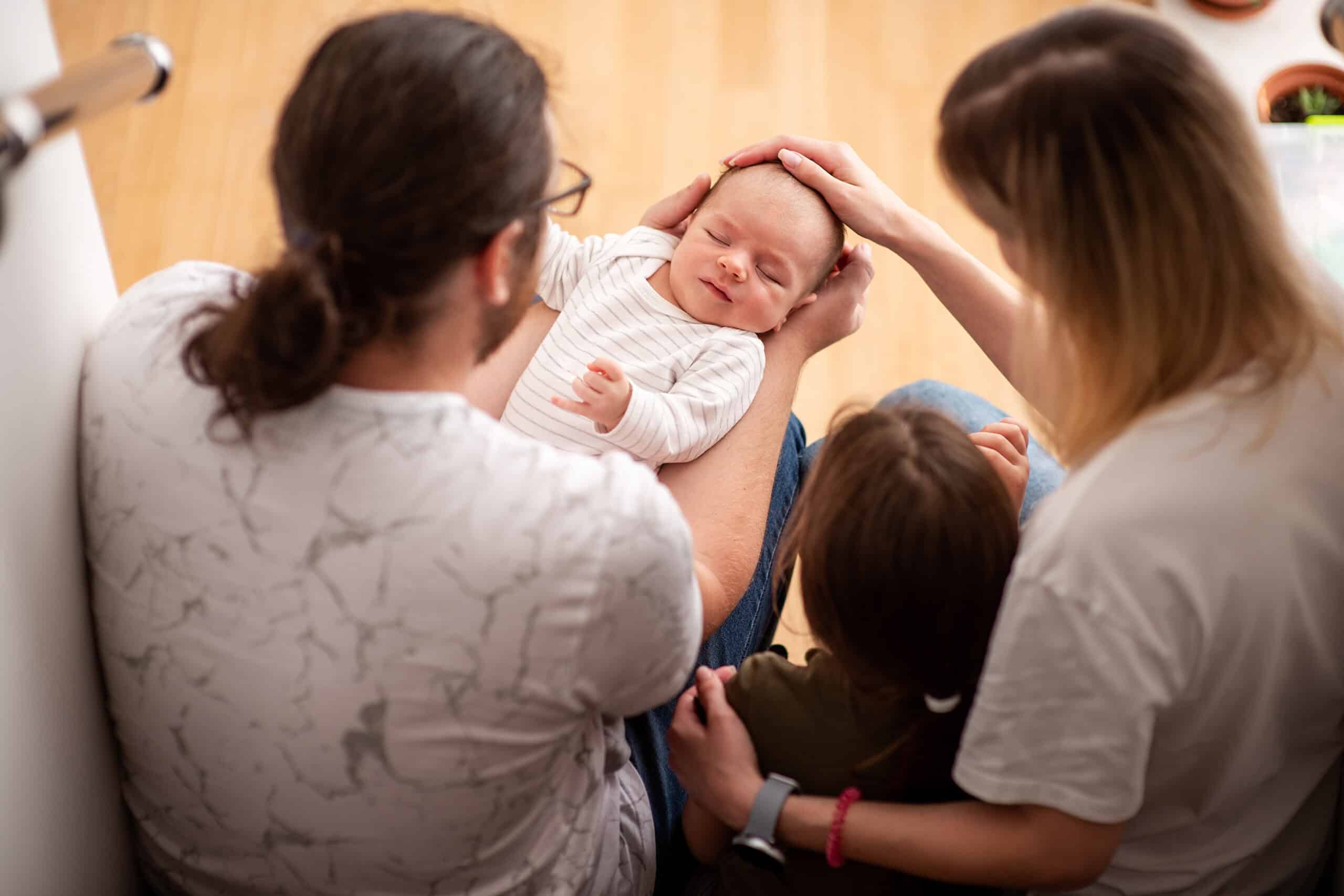 family admiring newborn baby sleeping in father's arms