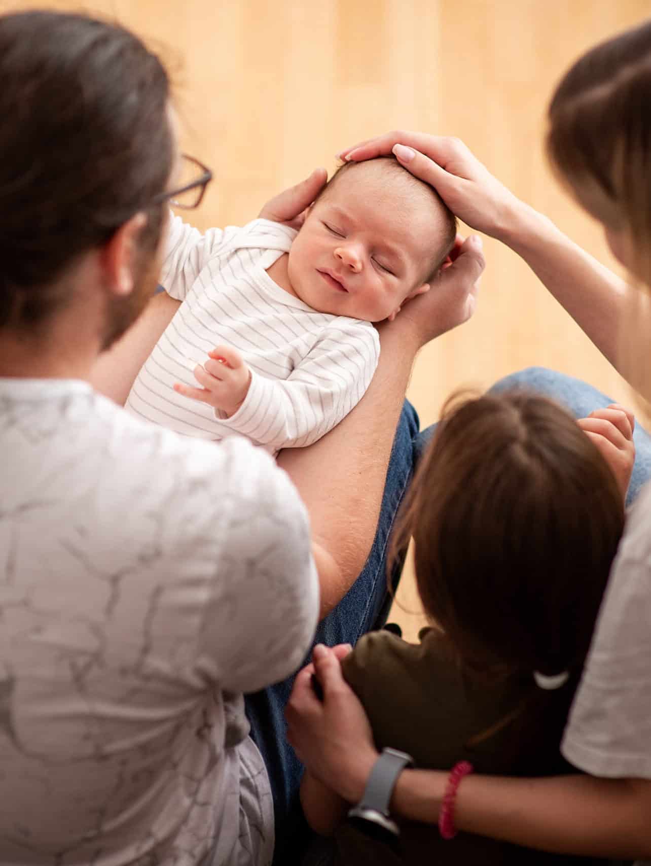 family admiring newborn baby sleeping in father's arms